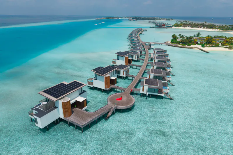 Aerial view of modern overwater villas with solar panels on wooden walkways at Crossroads Maldives resort, turquoise lagoon