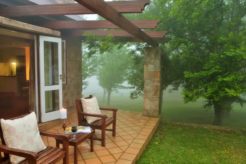 Cozy outdoor patio at Walkersons Hotel & Spa with cushioned chairs, wine glasses, candle on table, misty garden view.