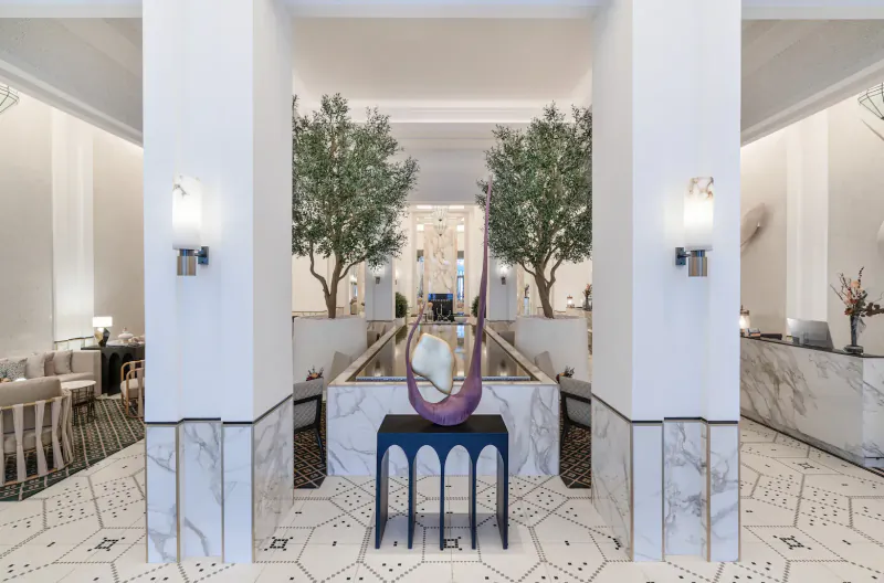 Fairmont La Marina Rabat-Salé Hotel lobby with purple sculpture on pedestal, olive trees, white columns, and marble reception.