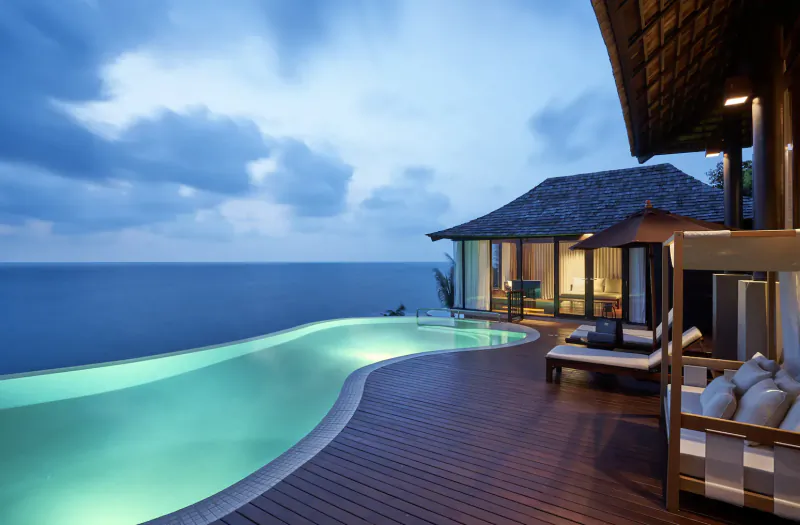 Twilight infinity pool overlooking ocean at Silavadee Pool Spa Resort, with wooden deck, loungers, and thatched villa.