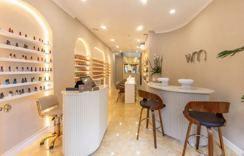 Modern Wumman nail spa interior in Fitzrovia with curved white reception, nail polish wall displays, and stylish seating.
