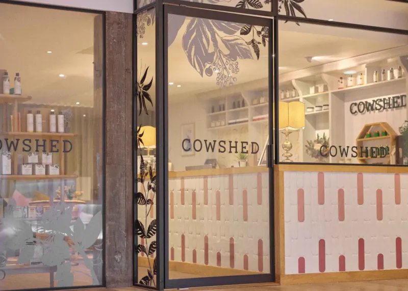 St Moritz Hotel Cow Shed café exterior with glass doors, plant decals, pink tiled counter, and 'COWSHED' signage.