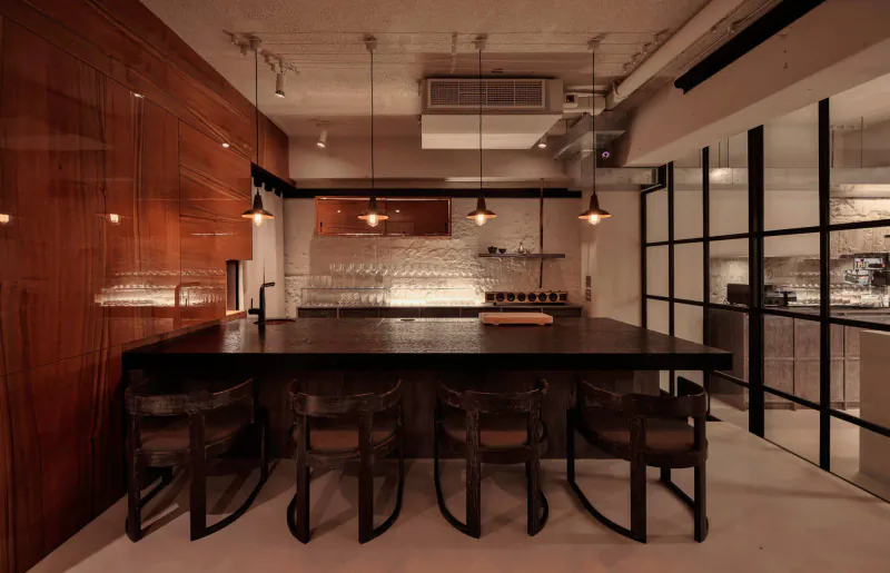 Stylish contemporary restaurant kitchen with wooden walls, black central island, bar stools, pendant lights, and glassware.