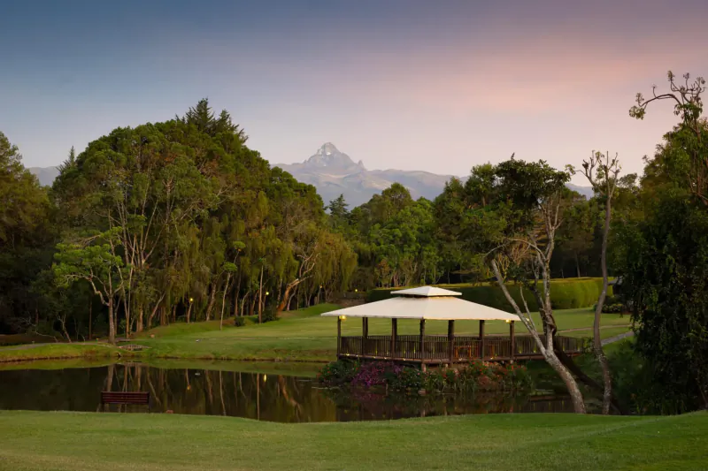 Fairmont Mount Kenya Safari Club: gazebo by pond on golf course with Mt Kenya peak at sunset, lush trees surround.