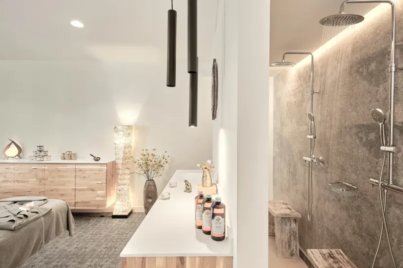 Modern spa bathroom in Baobab Suites resort with wooden vanity, hanging lamps, stone shower, towels, and lotions.