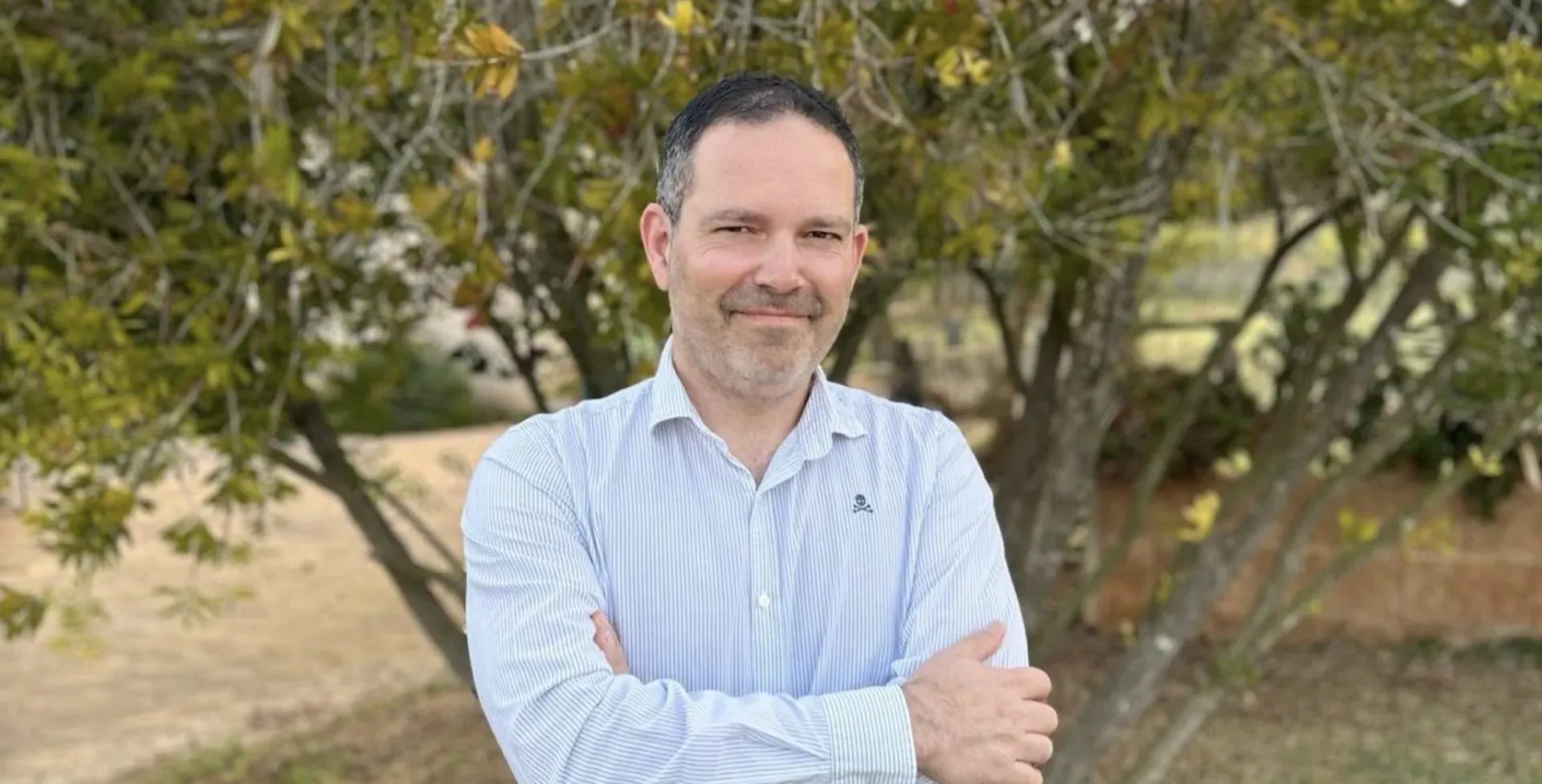 Jaume Alomar, GM of Son Penya Mallorca, smiling with arms crossed outdoors amid green trees