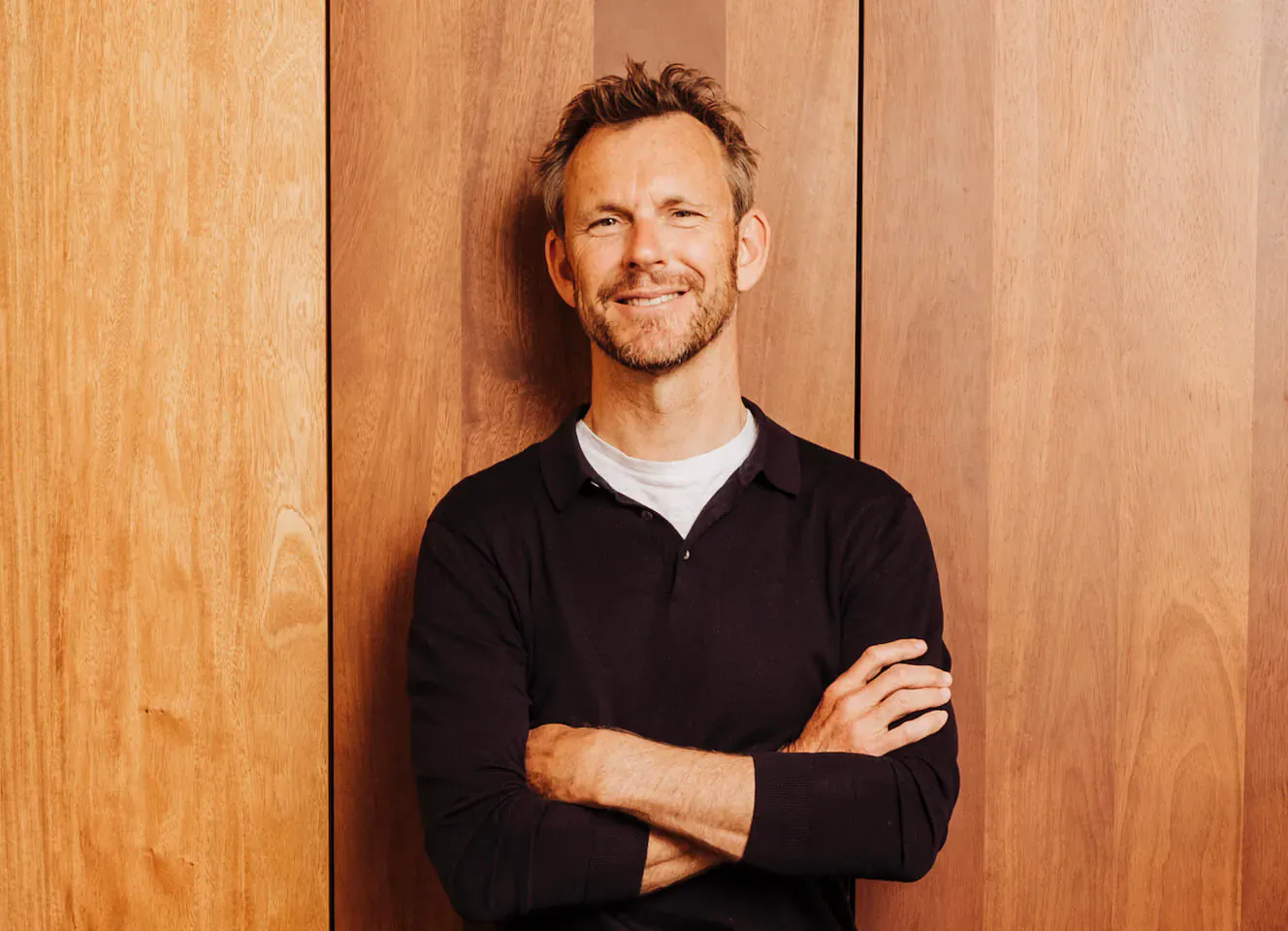 Filip Hoste of Baobab Suites smiling with arms crossed against wooden wall
