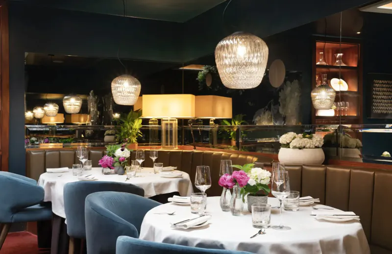 Elegant dining room at Pied à Terre with curved blue chairs, white tablecloths, pink flowers, wine glasses, and pendant lamps.
