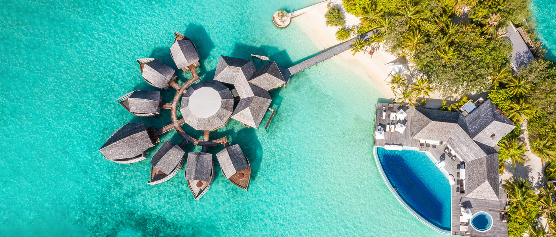 Aerial view of Lily Beach Resort overwater bungalows on turquoise lagoon with infinity pool and beach.