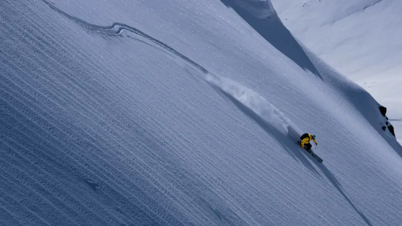 Skier in yellow jacket carving down a steep snowy mountain slope