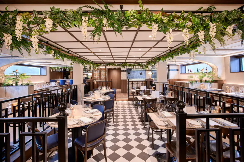 Elegant river cruise dining room with checkered floors, blue chairs, white tablecloths, and lush greenery garlands.
