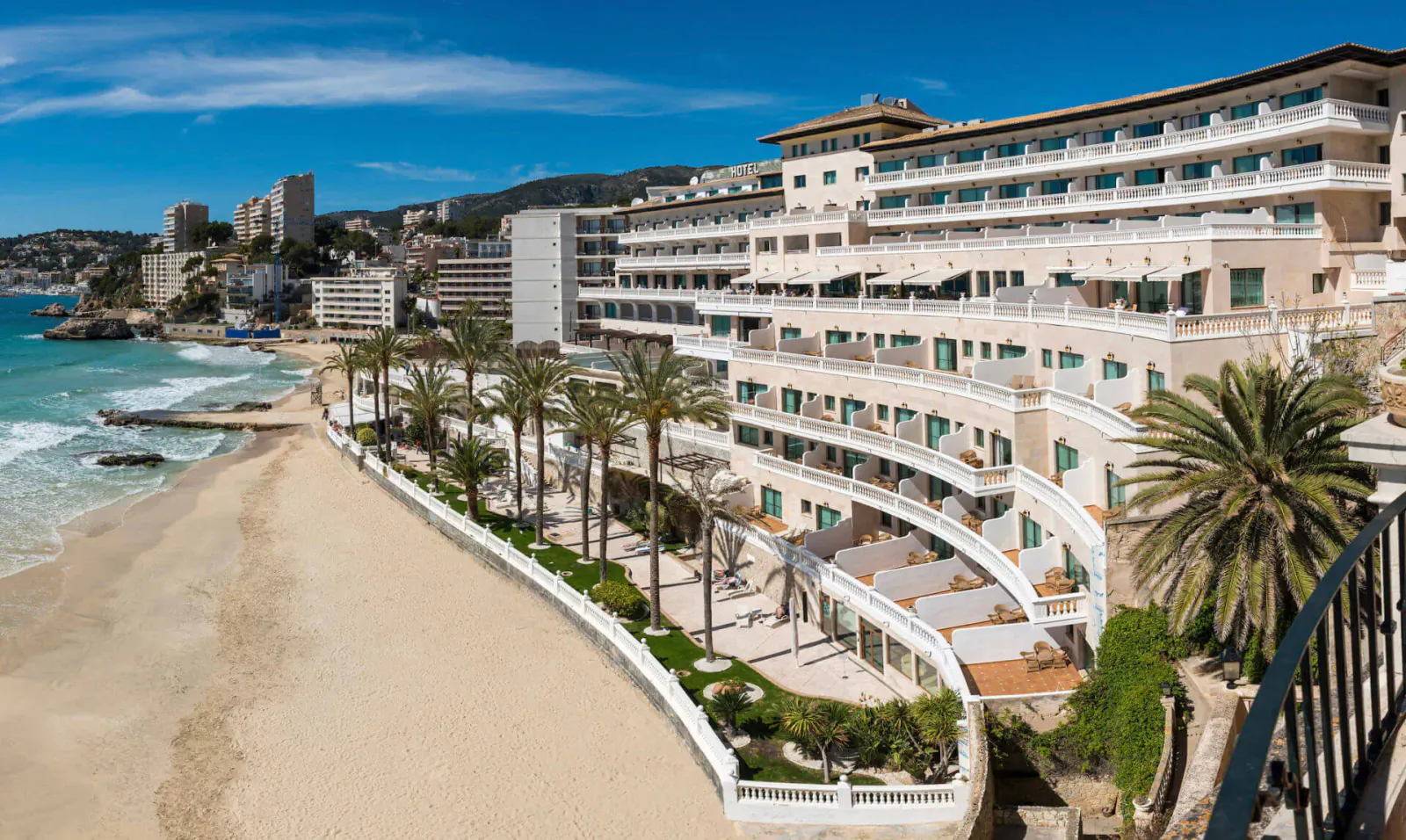 Aerial view of Nixe Palace luxury hotel on sunny beachfront with palm trees, ocean waves, and city skyline.