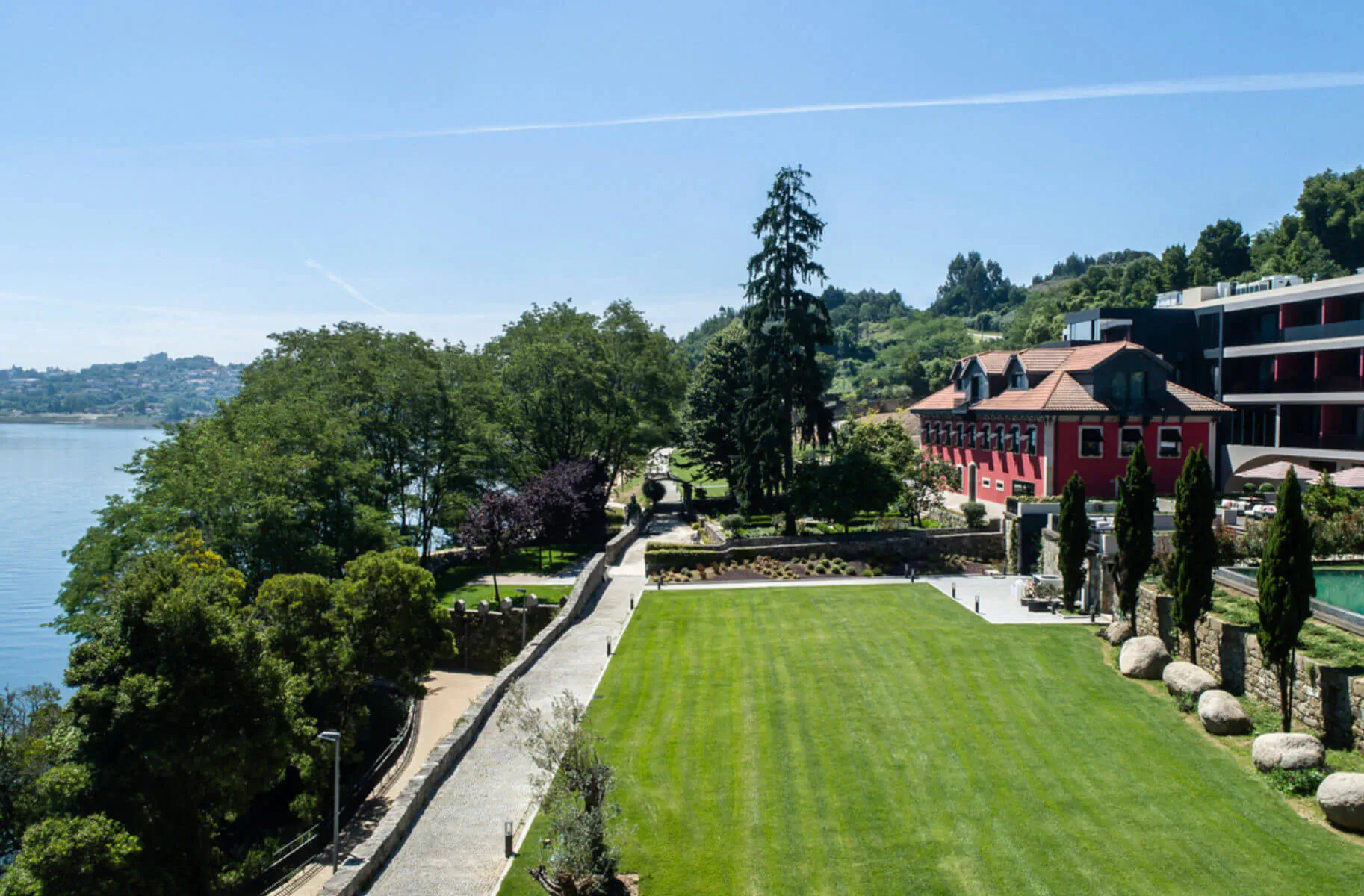 Aerial view of Vinha Boutique Hotel in Porto: red rooftops, lush gardens, lawns, pool, and Douro River.