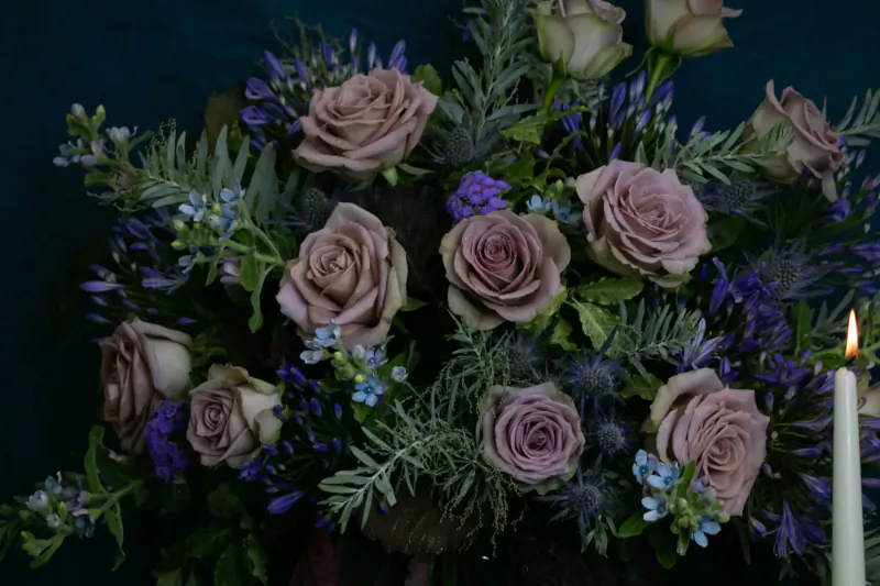 Elegant bouquet of mauve roses, lavender sprigs, and purple flowers with lit candle on dark background