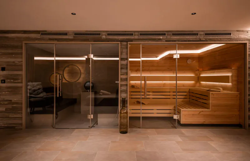 Modern wooden sauna room with glass doors, benches, and ambient LED lighting in luxury chalet spa.