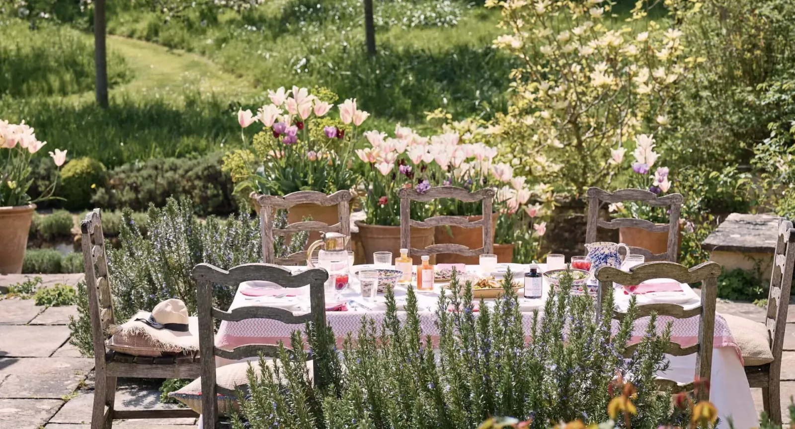 Elegant outdoor garden table set for a quintessentially English cordial celebration with pink tulips, rosemary, and glassware.