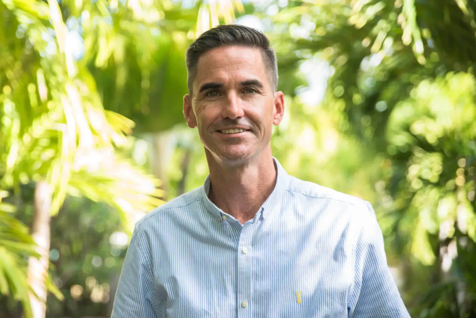 Brian Murphy smiling in light blue button-up shirt amid lush tropical greenery