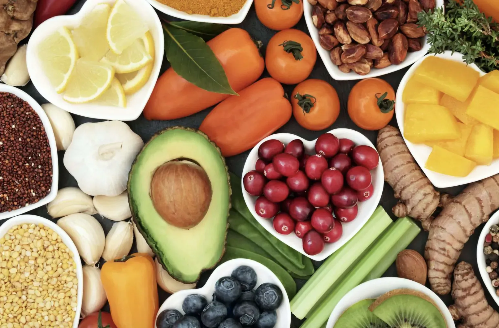 Vibrant assortment of fresh fruits, vegetables, nuts, and herbs arranged in heart shape on dark surface