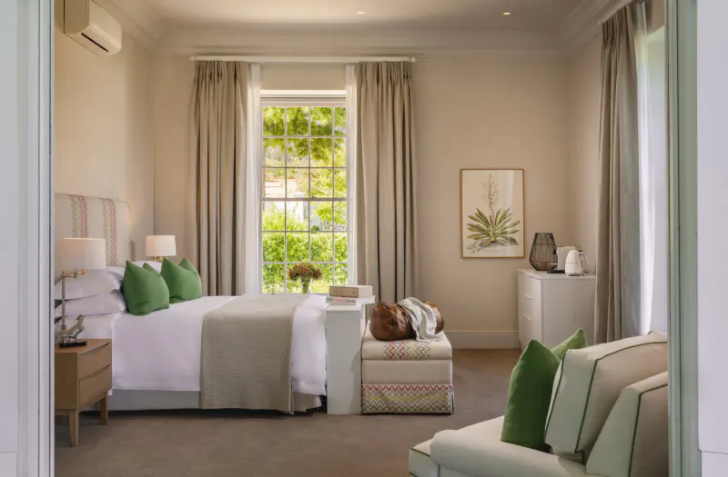 Elegant bedroom at Brookdale Wine Estate with green pillows on king bed, large window with garden view, neutral tones.