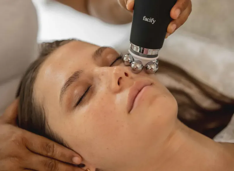 Therapist using Facsy microcurrent facial roller on relaxed woman's face at spa