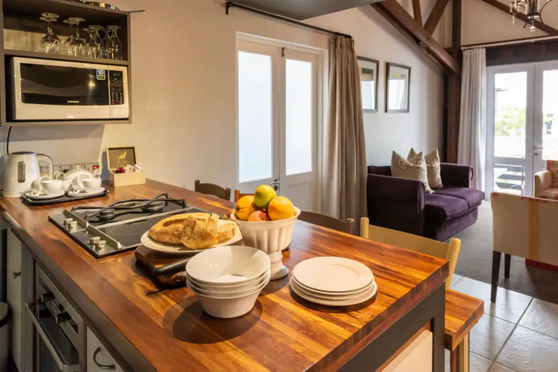 Modern kitchen island with stacked plates, bread platter, fruit bowl, and open-plan lounge at The Lofts Boutique Hotel.