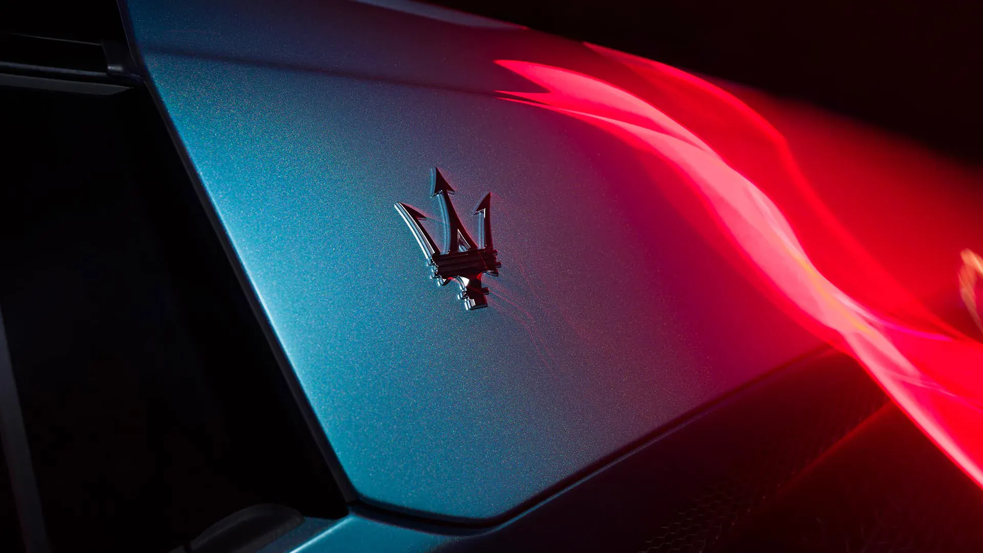 Close-up of Maserati trident logo on blue car side with dynamic red light trails