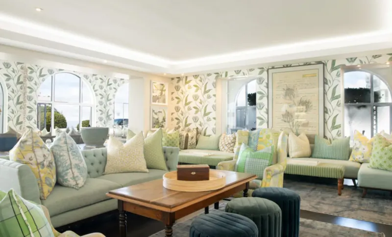 Elegant lounge at The Marine Hotel Hermanus with green floral wallpaper, plush green sofas, and wooden coffee table