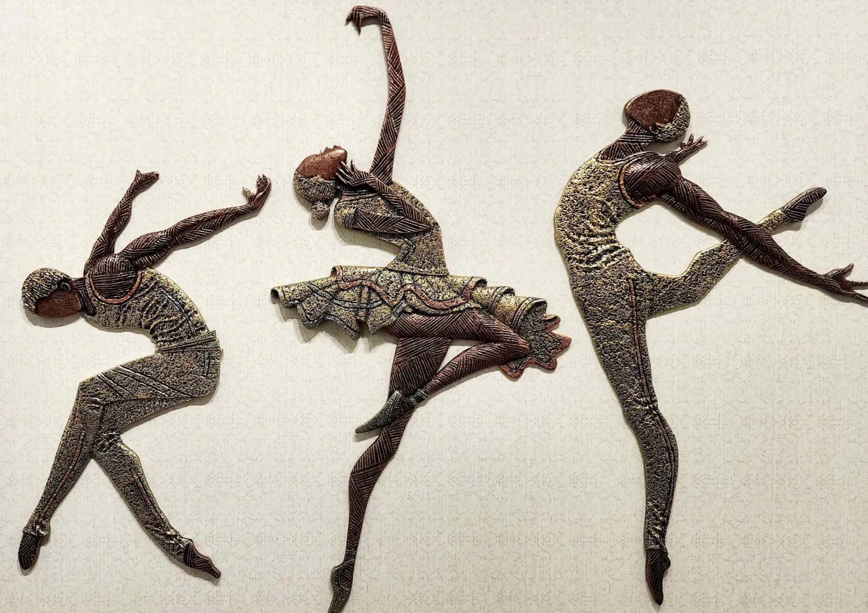 Three textured bronze ballerinas in dynamic dancing poses on white background