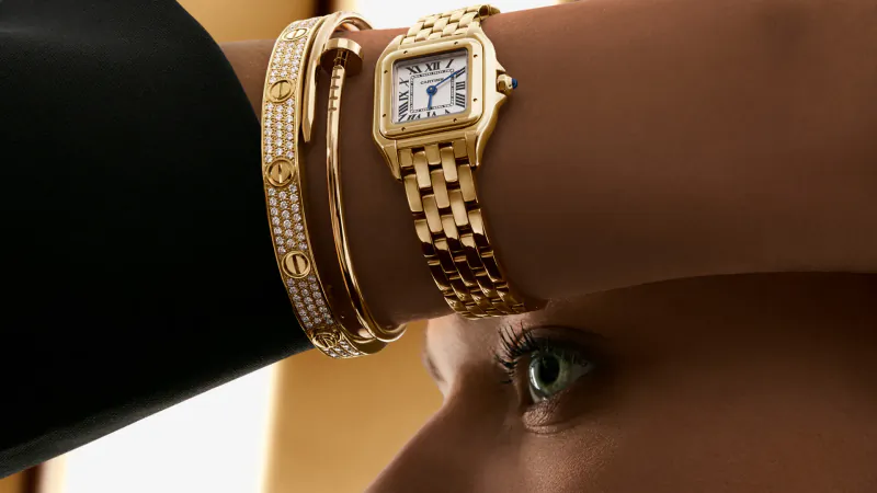 Close-up of woman's wrist with gold Cartier Panthère watch and diamond bracelet, green eye visible.