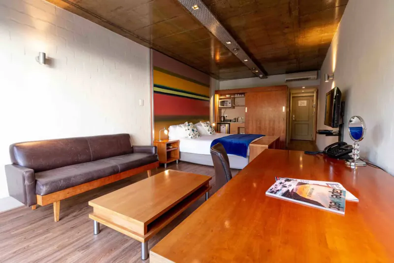 Modern hotel room at Hippo Boutique Hotel with leather sofa, wooden desk, blue bed, and colorful striped wall.