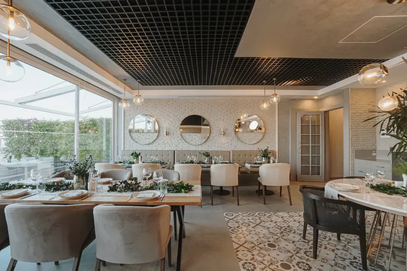Elegant dining room in luxury Turkish resort with wooden tables set for meals, beige chairs, mirrors, plants, and garden view.