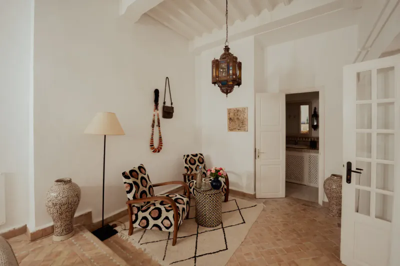 Cozy Moroccan villa living area with patterned armchairs, brass lantern, terracotta floor, and white walls in Essaouira.