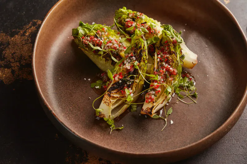 Grilled endive spears topped with green herbs and red sauce in a brown bowl