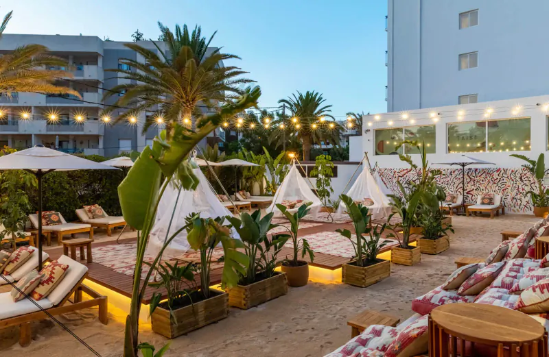 Hotel Riomar Ibiza poolside terrace with white tipis, loungers, palms, and string lights at dusk.