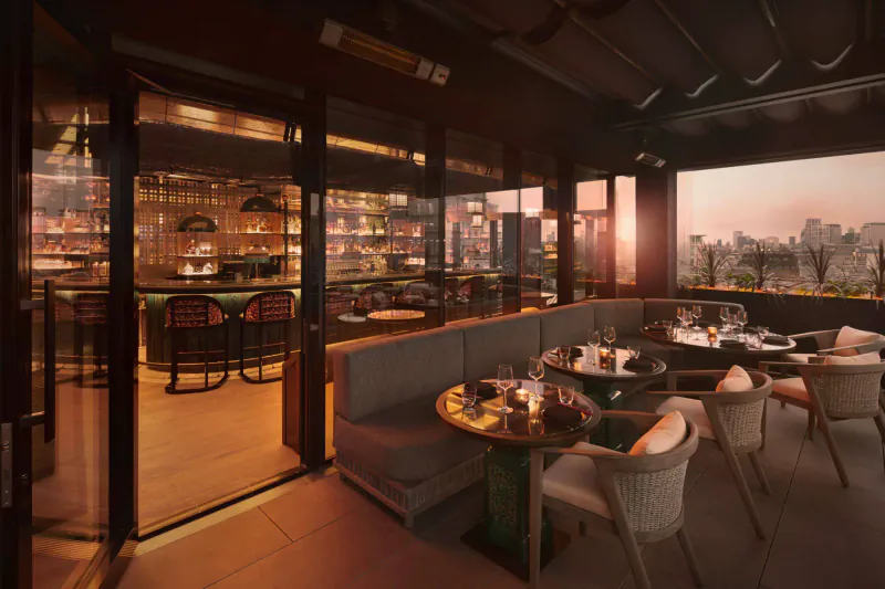 Elegant rooftop bar at Tattu London with warm lighting, liquor shelves, plush seating, cocktails, and city skyline sunset view.