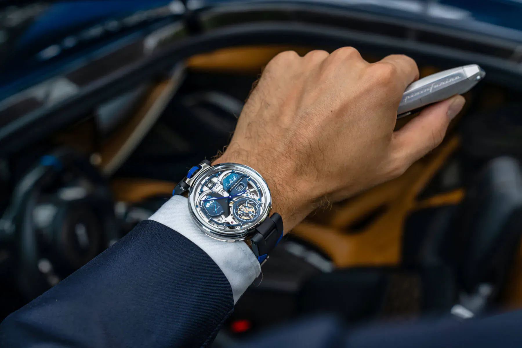 Man's hand wearing BOVET Battista Tourbillon watch with blue dial and strap, holding key fob in luxury car interior.
