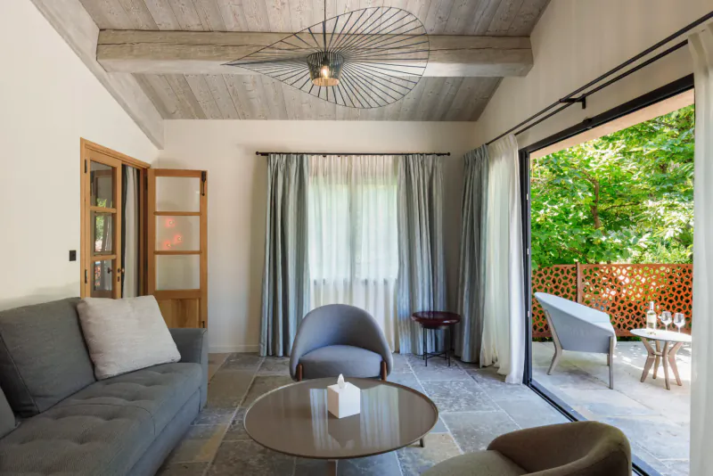 Cozy lounge in Lou Calen Boutique Hotel, Provence: gray sofa, armchairs, wood beam ceiling, fan light, garden view.