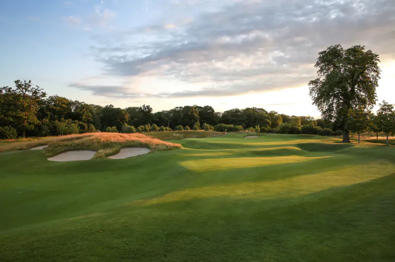 Aerial view of lush green golf course with bunkers and trees at sunset during The Grove tournament
