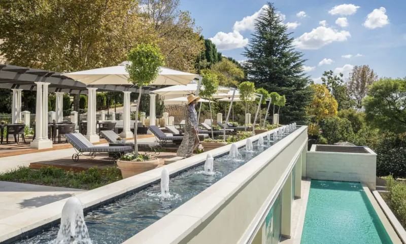 Rooftop pool terrace at Four Seasons Hotel The Westcliff, Johannesburg, with loungers, umbrellas, fountains, trees, and city view.