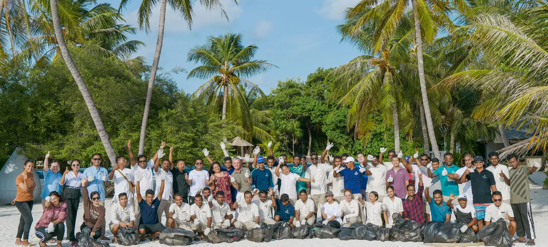 Group photo of Hideaway Beach Resort & Spa team with Parley Maldives for ocean campaign, posing amid palm trees on beach