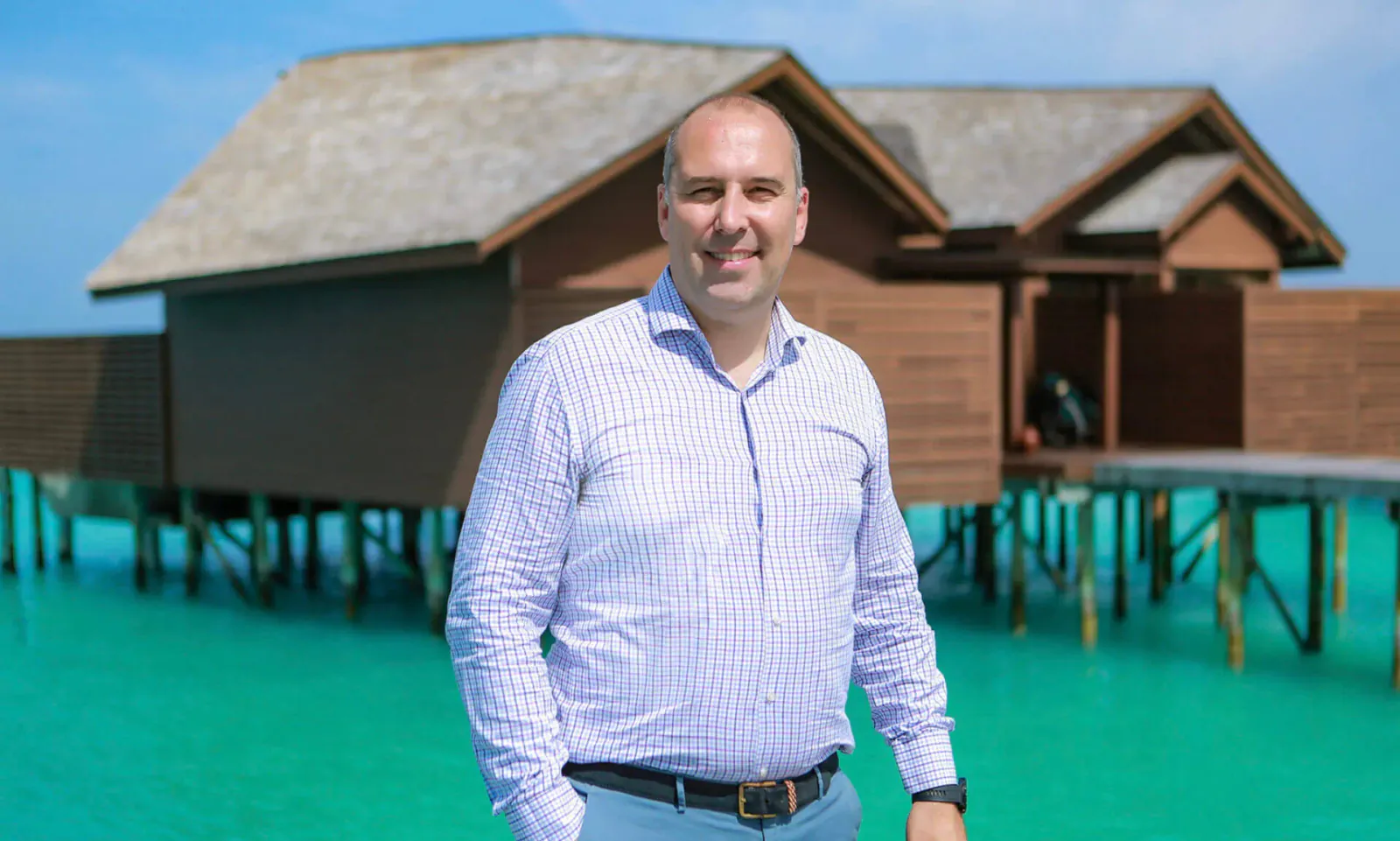 Desislav Gospodinov smiling in light blue shirt in front of Lily Hotels' overwater villas on turquoise lagoon
