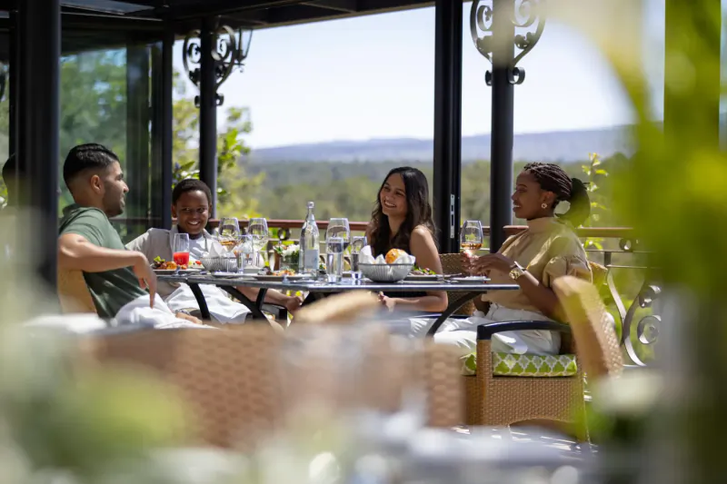 Diverse group of four enjoying drinks and appetizers at an elegant outdoor terrace table with mountain view.