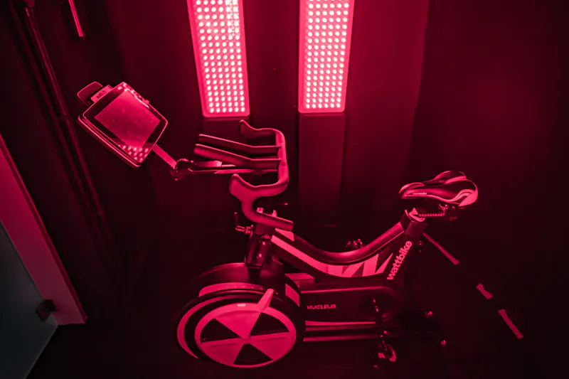 Black Peloton-style spin bike with red LED panels in dark gym, angled view