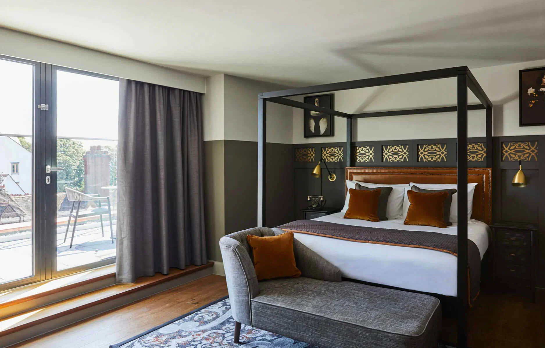 Elegant bedroom in Hotel Indigo Chester with black four-poster bed, velvet pillows, armchair, and city view windows.