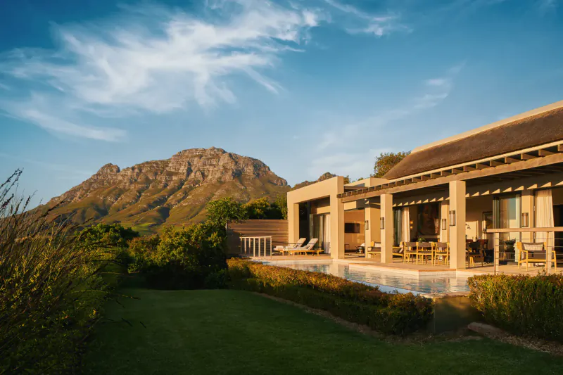 Luxury modern house with infinity pool and terrace at Delaire Graff Estate, overlooking Cape Winelands mountains at sunset.
