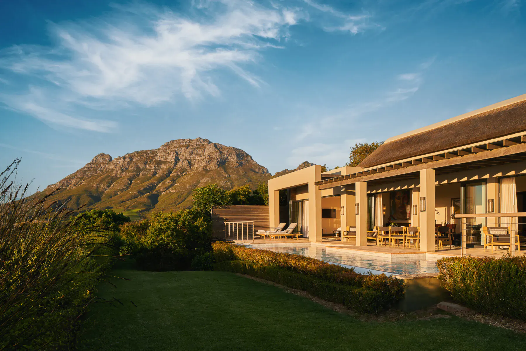 Luxury modern house with infinity pool and terrace at Delaire Graff Estate, overlooking Cape Winelands mountains at sunset.