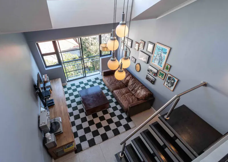 Top-down view of modern loft lounge at Hippo Boutique Hotel: brown leather sofa, checkered floor, pendant lights, art walls, large windows, stairs.