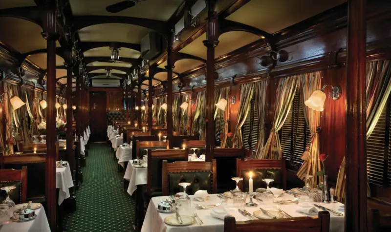 Luxurious wooden-paneled Rovos Rail dining car with candlelit tables, green carpet, and curtains.