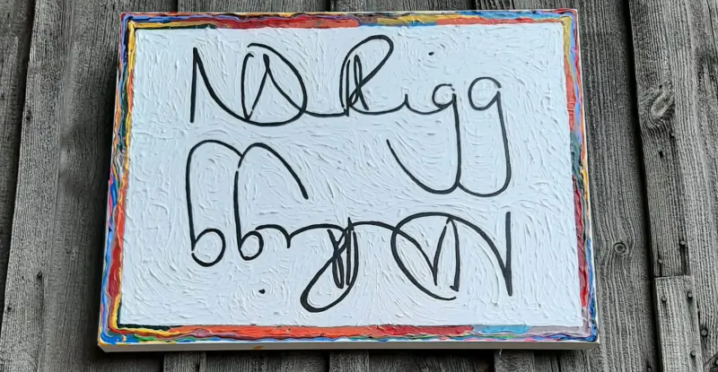 Handwritten 'ND Rigging' on white textured plaque with rainbow frame, mounted on wooden wall