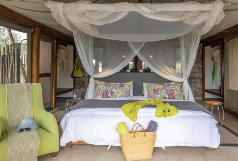 Luxurious king bed with white canopy and colorful pillows in safari lodge tent at Onguma, Etosha, with yellow beach bag.